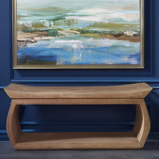 Wooden entryway bench that is skinny with storage with art above in a blue hallway.