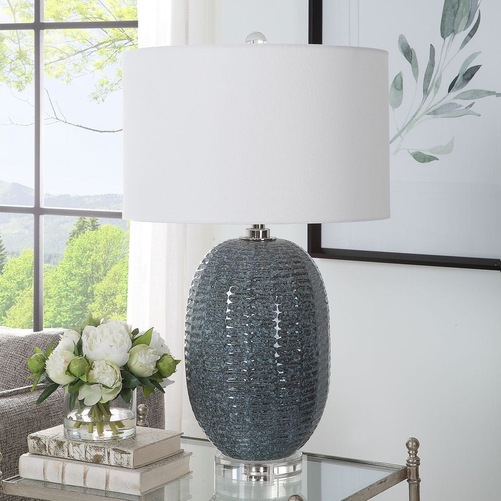 Decorative lamp with textured base on a table in a room with a window and plant.