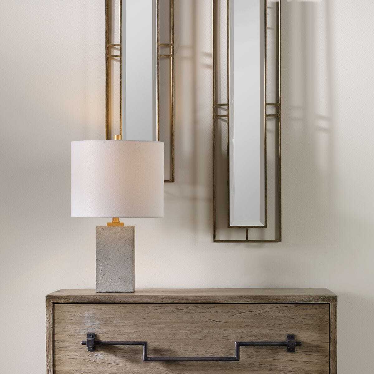 Table lamp with a white shade and gray base on a wooden console table, with a mirror in the background.