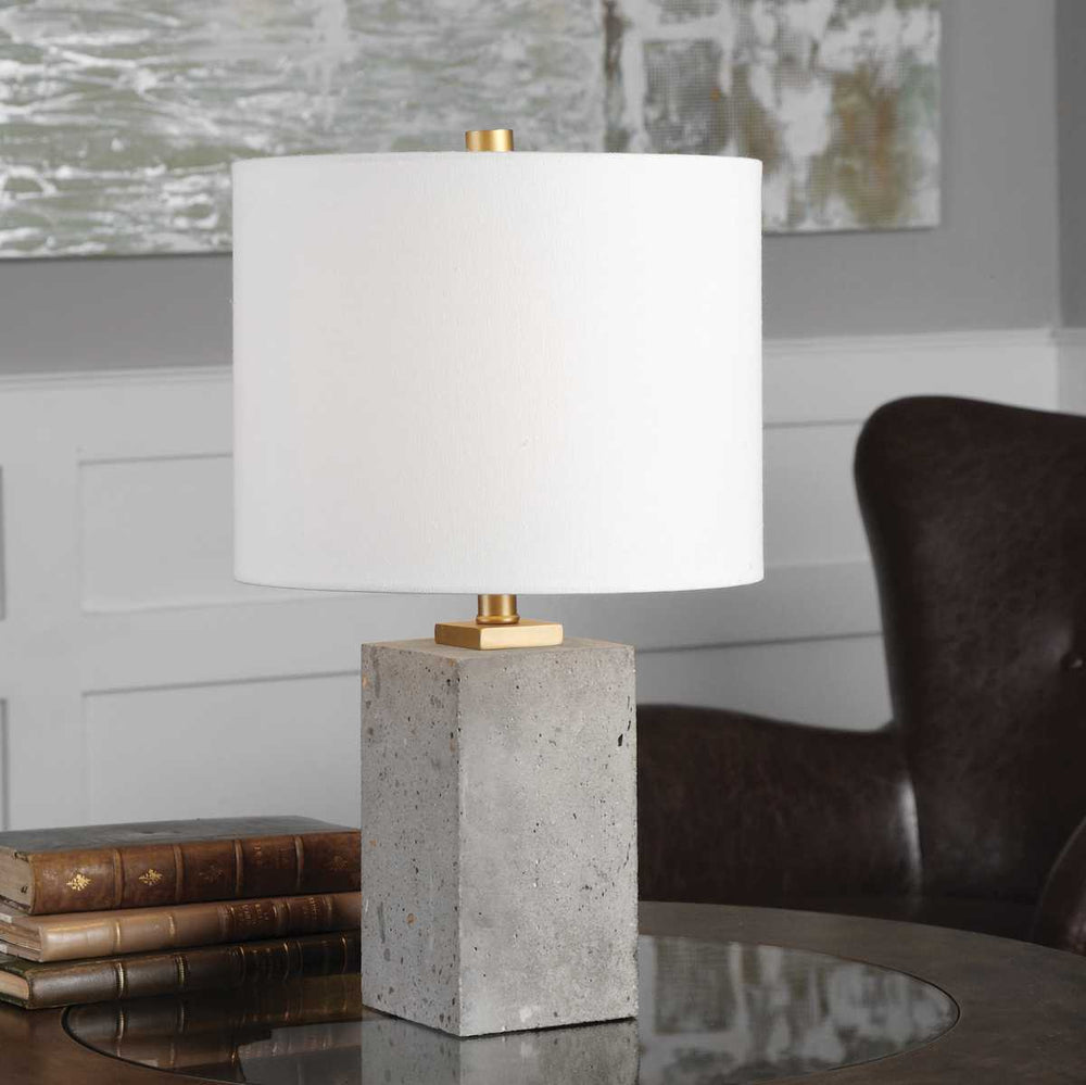 Table lamp with concrete base and white shade on a table in a room setting.