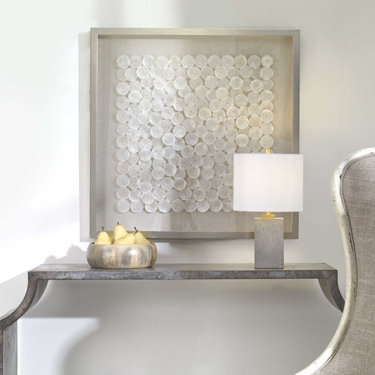 A shadow box style wall piece featuring natural layered capiz shells on a flax-toned linen backing, framed in pine wood with a brushed silver finish.