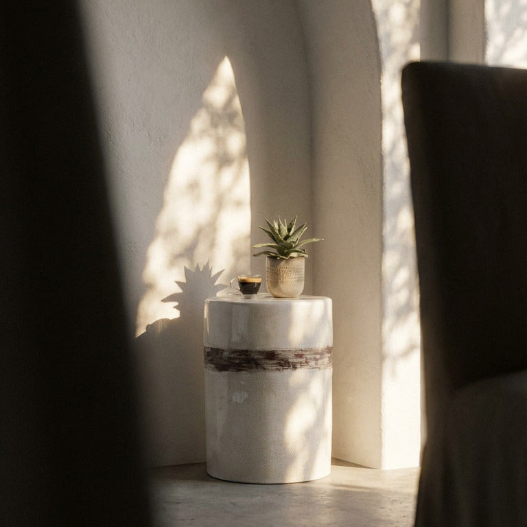 White pedestal table with a plant in a sunlit room with arched ceilings