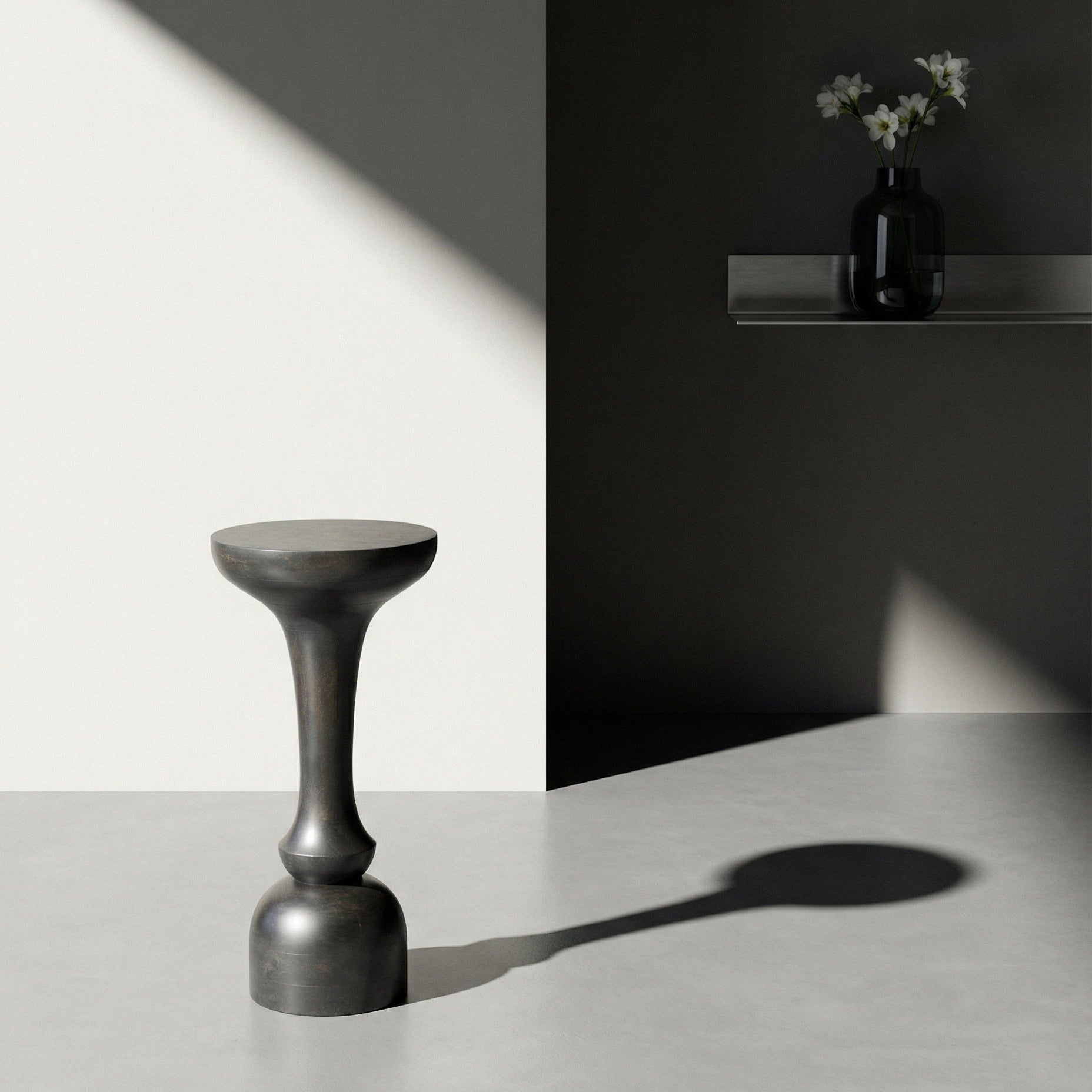 Dark gray stool on a light surface with a black wall and white flowers in the background