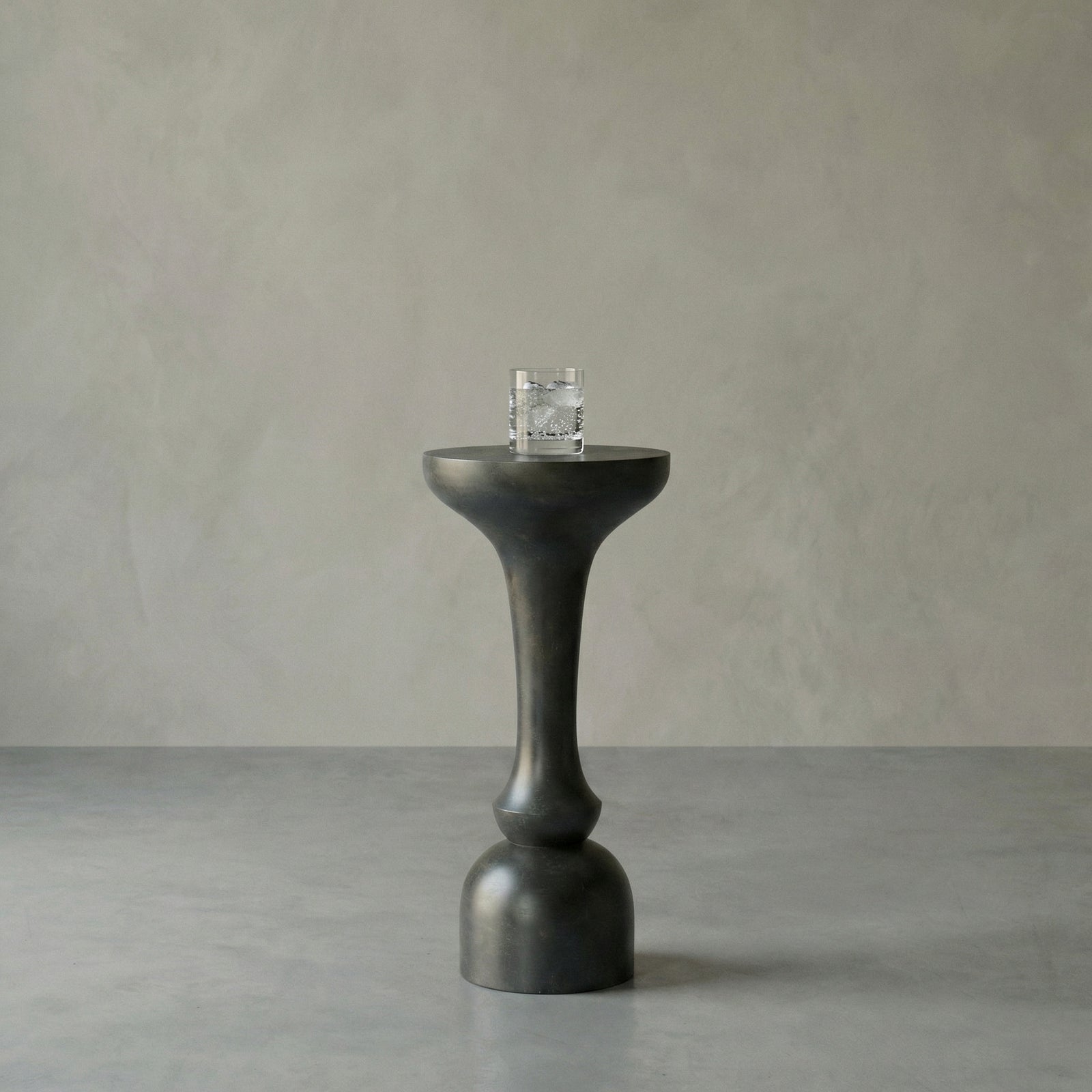 Black pedestal table with a glass on a gray background