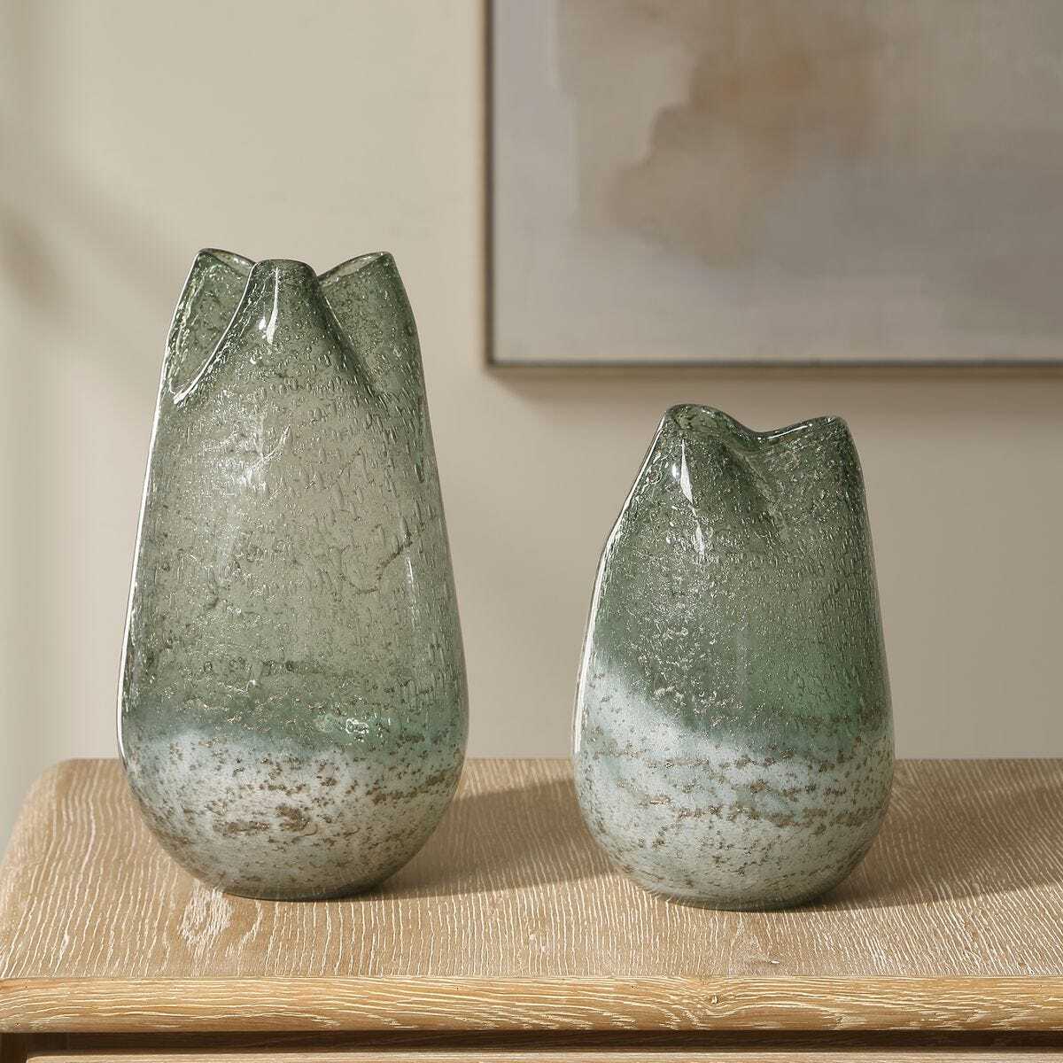 Two green glass vases on a wooden surface with a neutral background