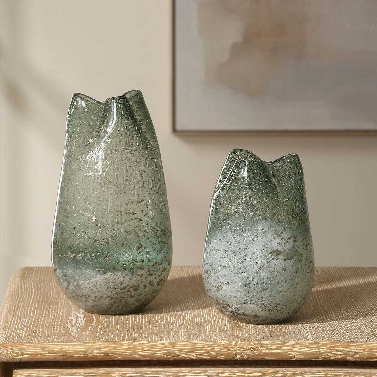 Two green glass vases on a wooden surface with a neutral background