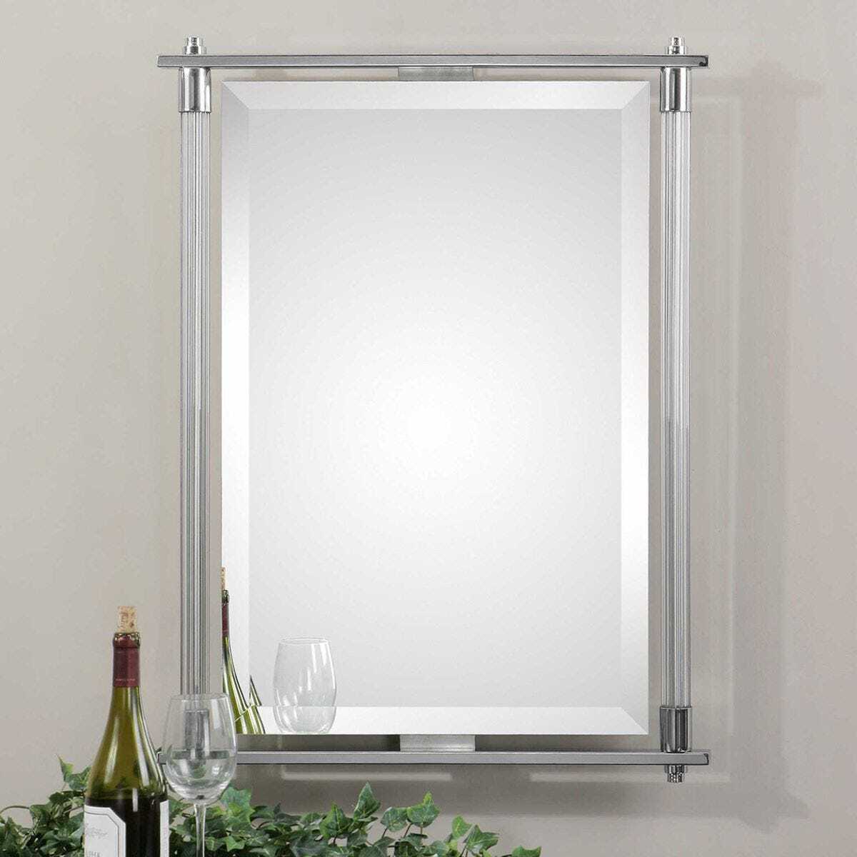 Rectangular mirror with a silver frame on a light gray wall, with bottles and glasses in the foreground.