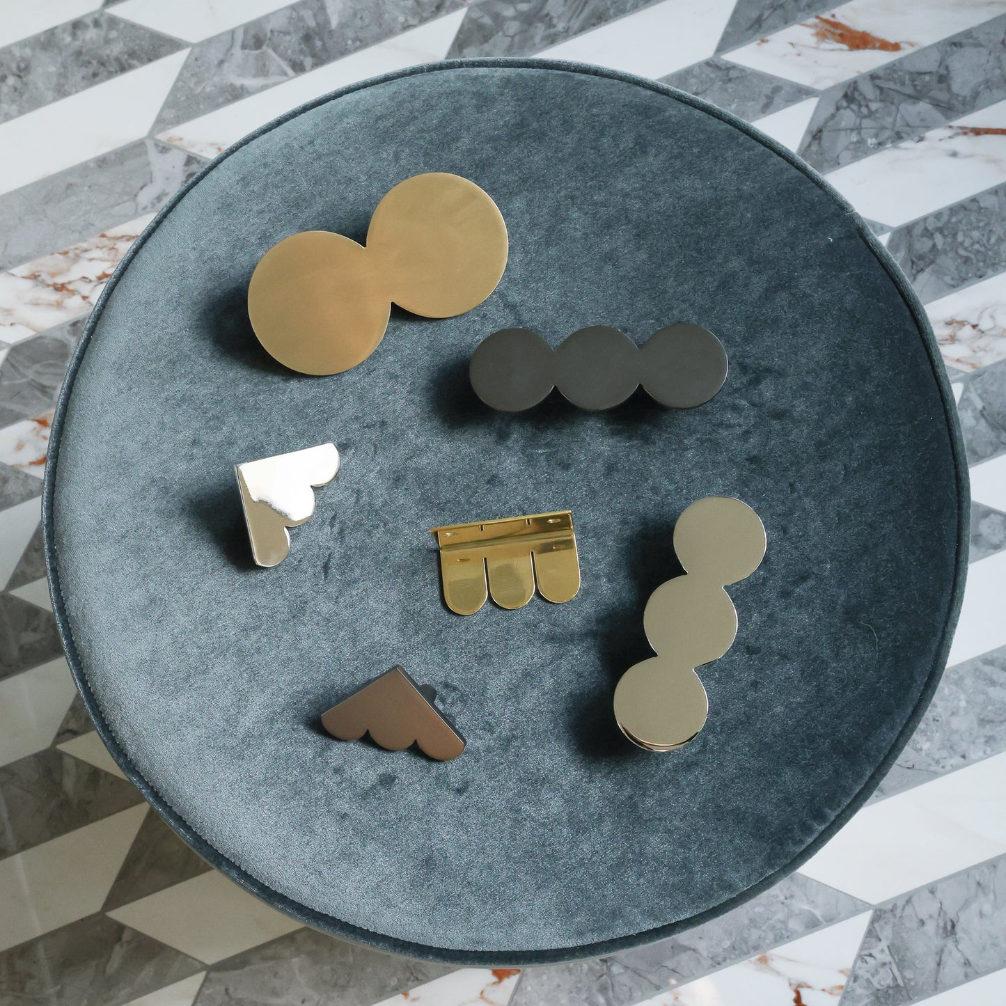 A top-down view of several oversized cabinet knobs and pulls arranged on a round blue-gray ottoman tray over a gray and white marble-patterned floor.