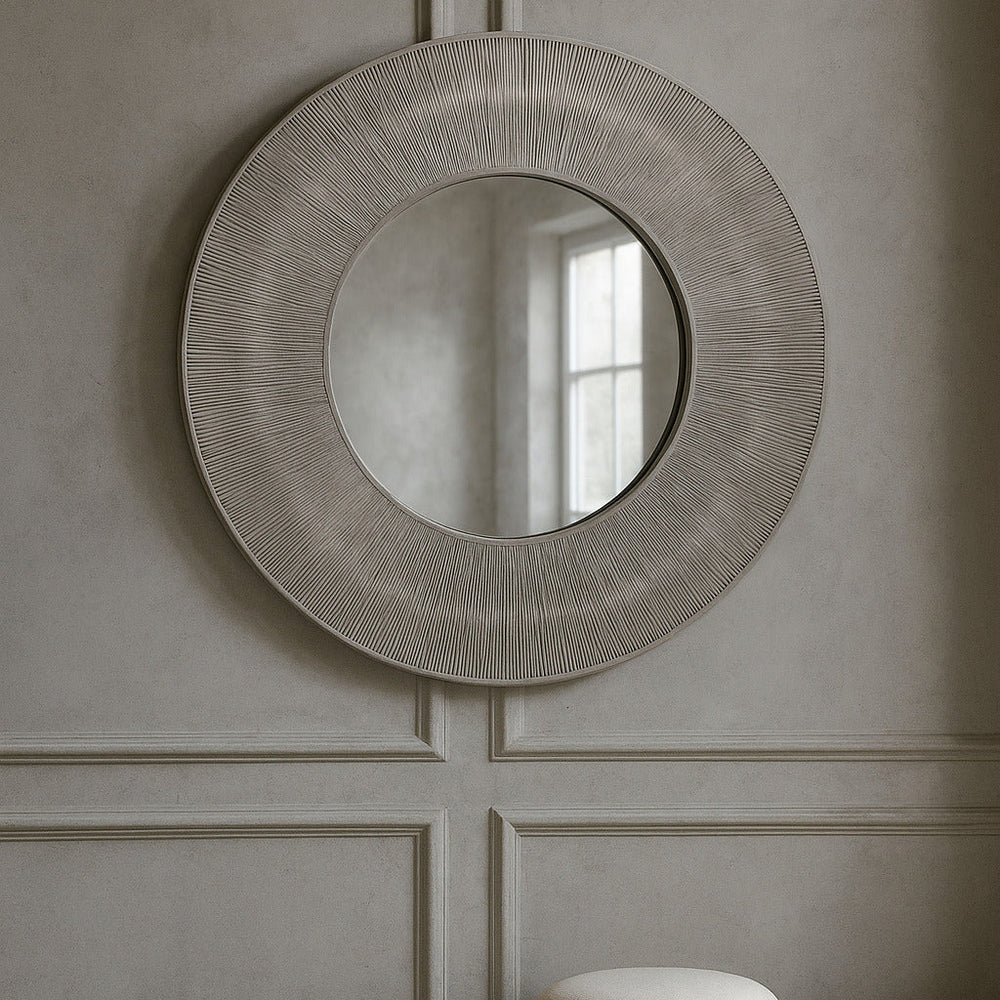 Round decorative mirror on a wall with wicker stools below