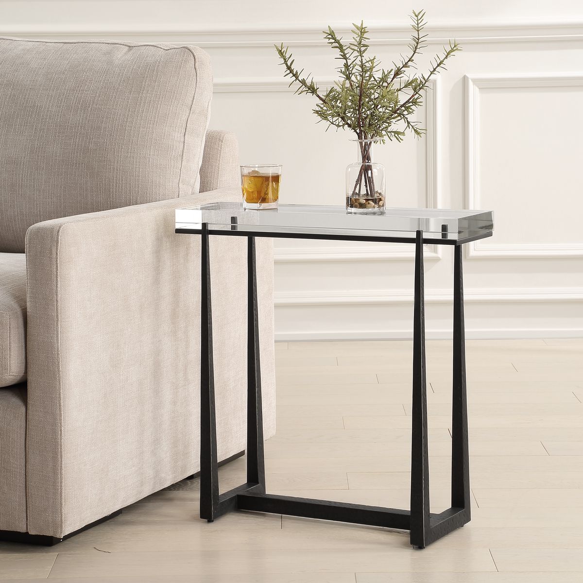 Clear side table with bronze crystal top rectangle next to sofa, decorated with a plant in vase on top of table.