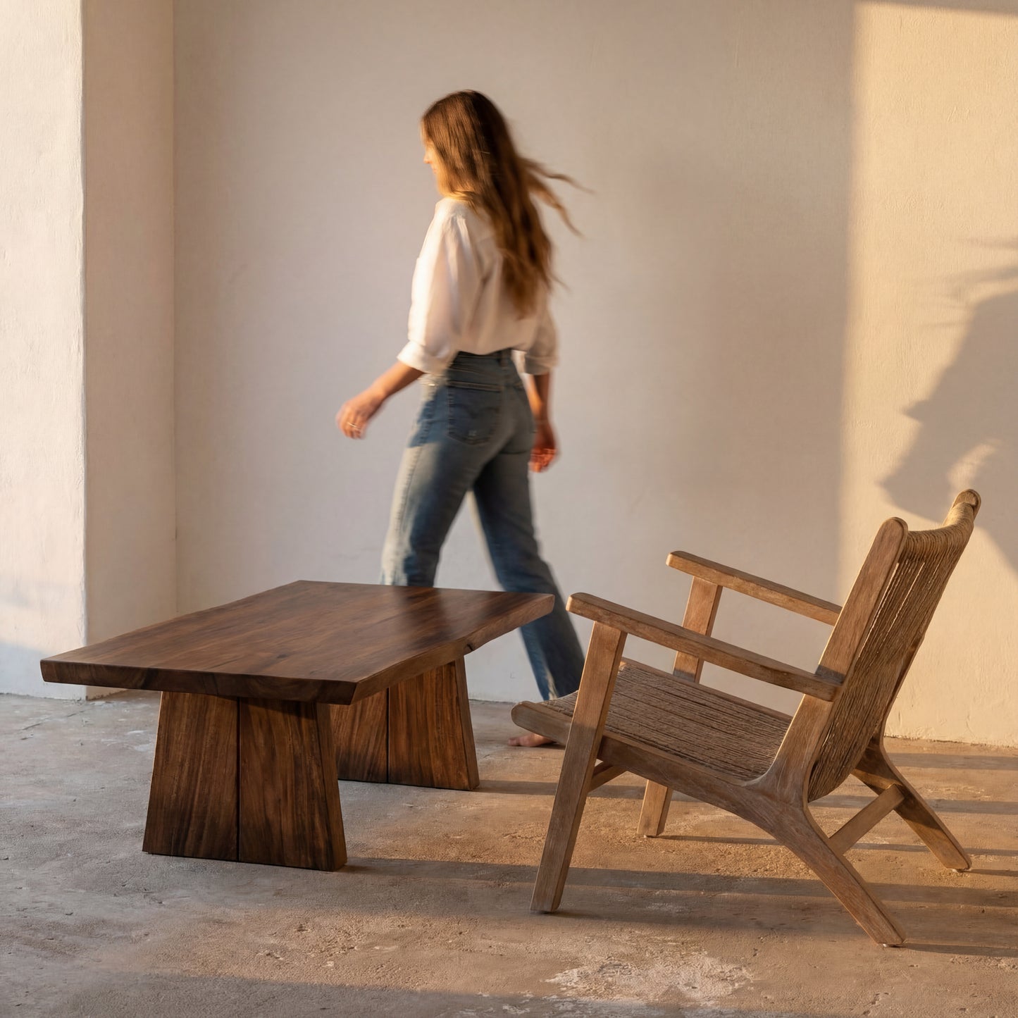 Wooden table and chair in a minimalistic setting with a person walking in the background.