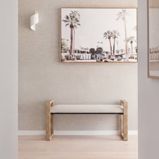 A modern bench with a light beige upholstered seat and a natural wood frame, shown in a minimalist white studio setting with a soft shadow.