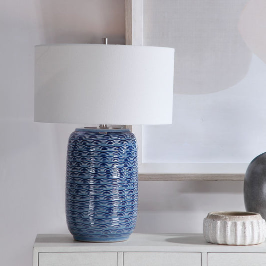 Coastal blue table lamp on white console and white bowl with neutral painting.