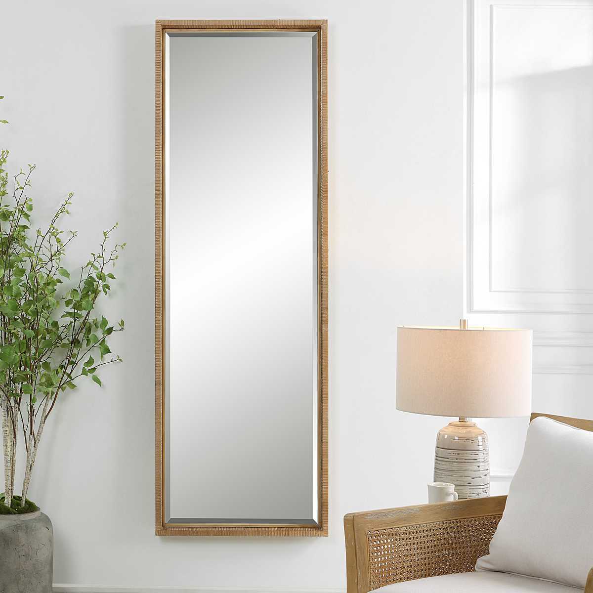 Wooden floor mirror on a white wall with a lamp and plant in the background