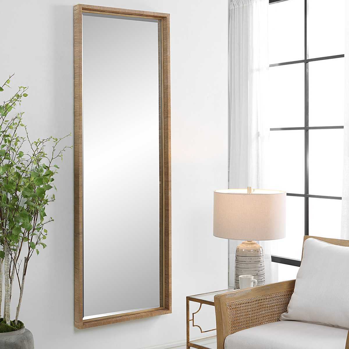 Full-length mirror with wooden frame on a white wall next to a chair and lamp.