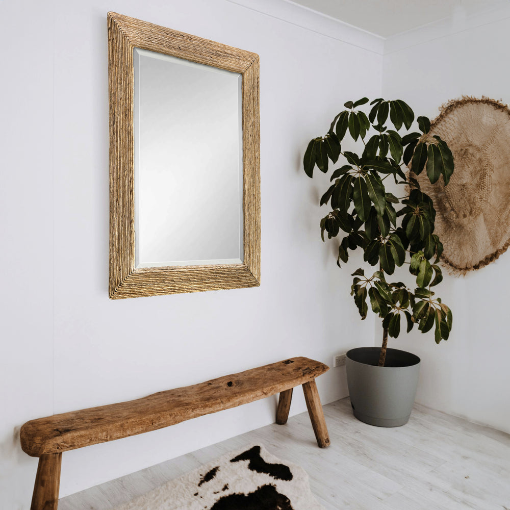 Large woven coastal mirror above wooden entryway bench in a white living room with a green plant in the corner.