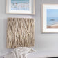 Coastal twig art on white wall with another beach print and white decorative bench in living room.