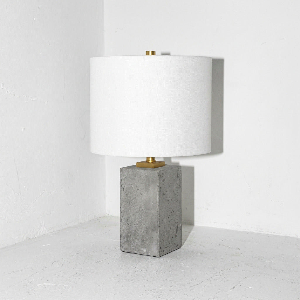 Table lamp with concrete base and white shade on a white floor.