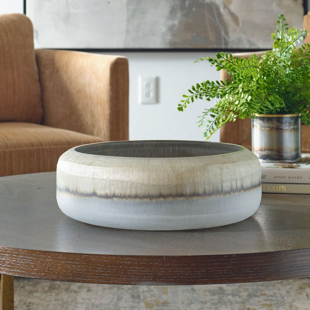 Empty contemporary decorative bowl in gray and white on a wood coffee table with brown chairs.