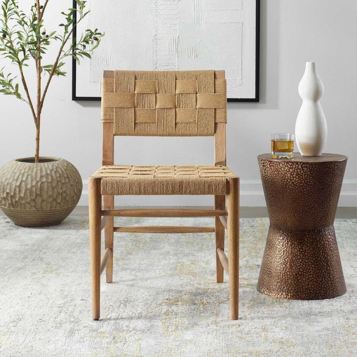 Woven chair next to a textured side table with a plant and decorative items in a room.