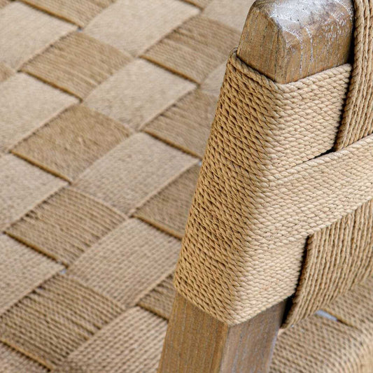 Woven chair next to a textured side table with a plant and decorative items in a room.