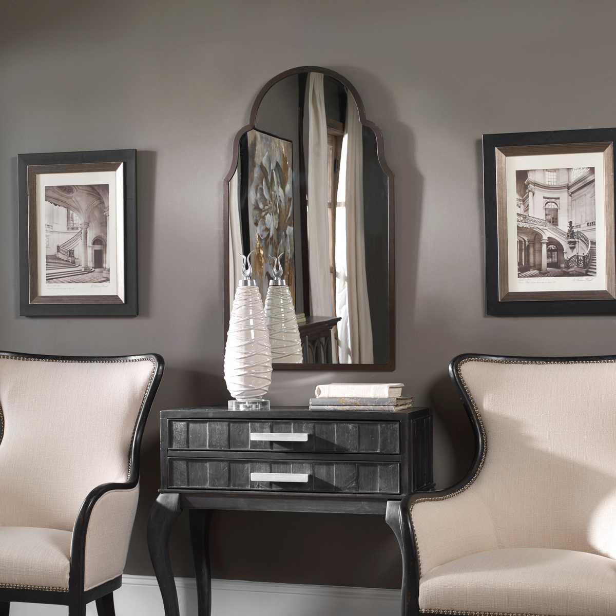 Decorative console table with mirror and chairs in a room with framed pictures on the wall.