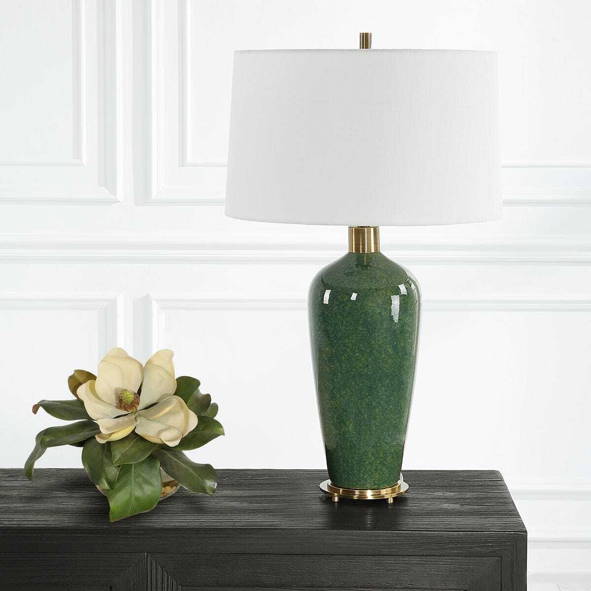 Green lamp with white shade on a dark surface against a white paneled wall