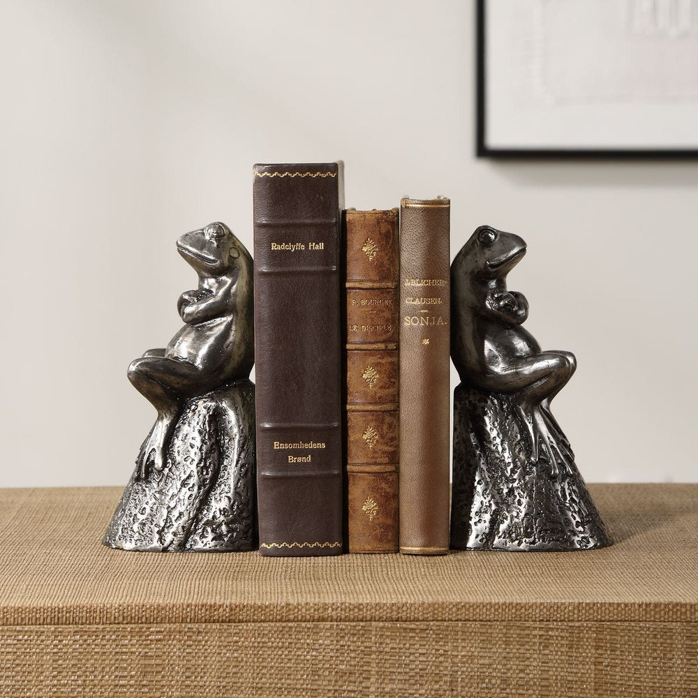 Decorative bookends shaped like frogs on a shelf with books.