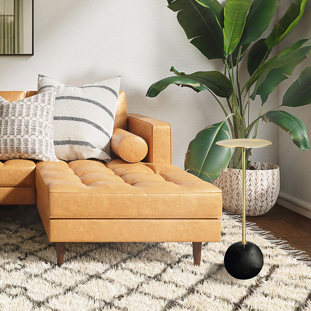 Black round marble base with brass stems and table surface next to a leather sofa and white carpet.