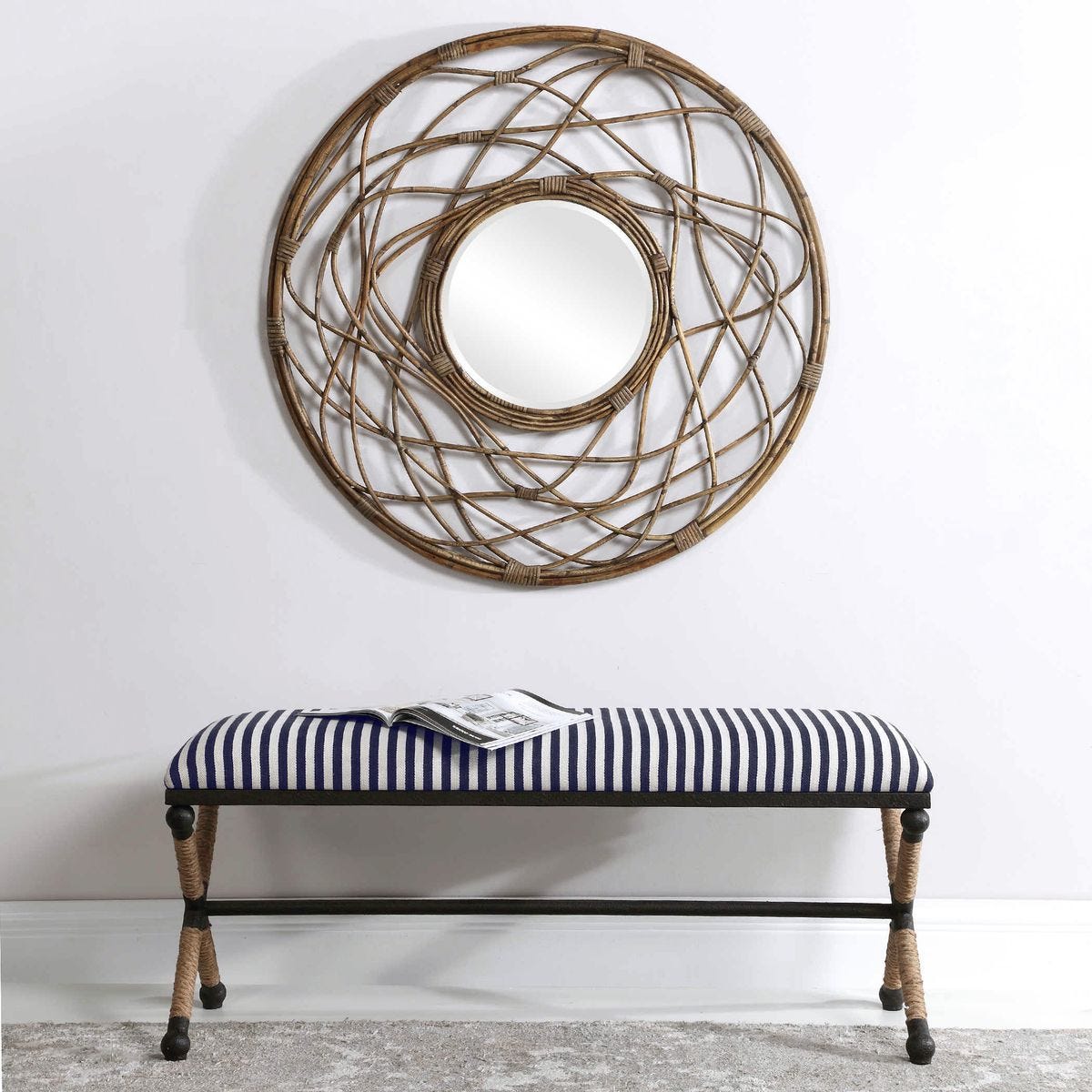 Decorative round mirror with wicker-like frame above a striped bench against a white wall.