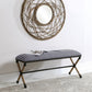 Striped bench with woven legs in front of a decorative wall mirror.
