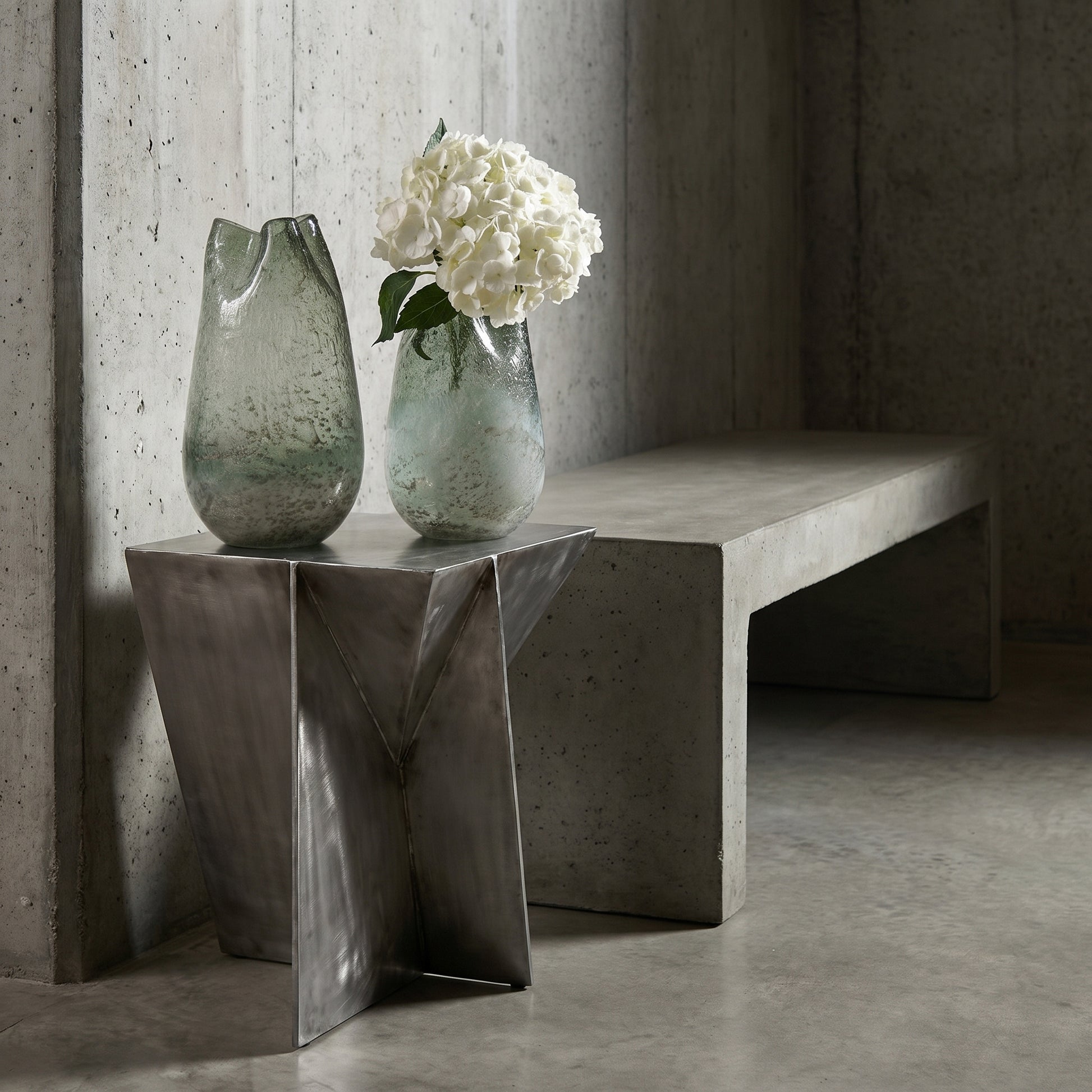 Two vases with white flowers on a modern concrete bench against a concrete wall.
