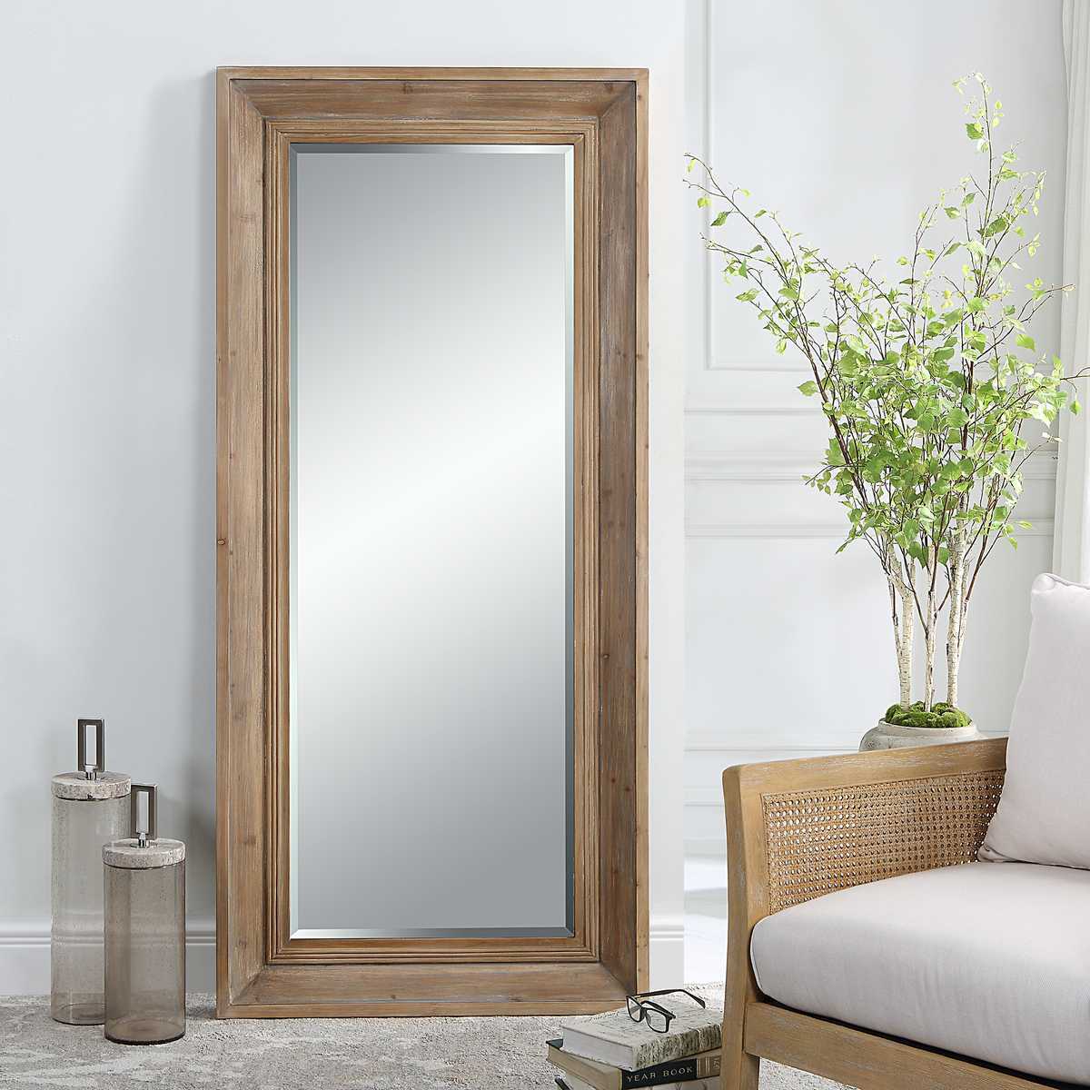 Wooden floor mirror in a room with a chair and decorative items.