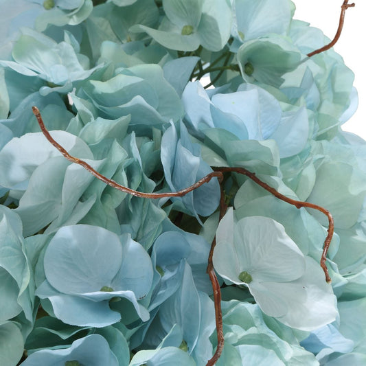 Light blue hydrangeas in clear vases on a table with a lamp and mirror in the background.
