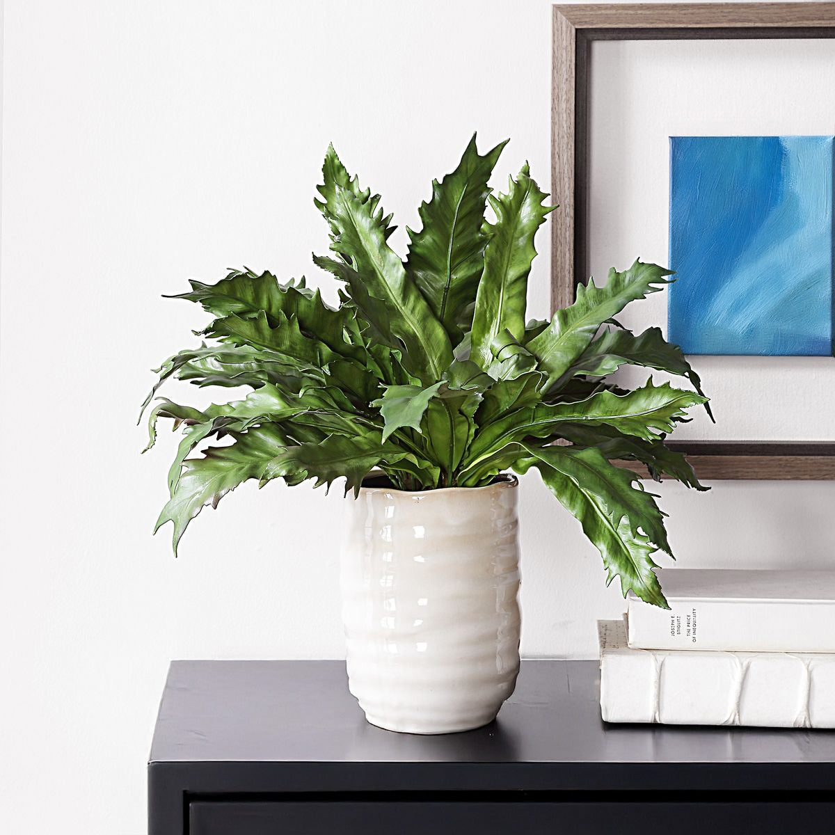 Ceramic tan plant with a faux fern on a black console.