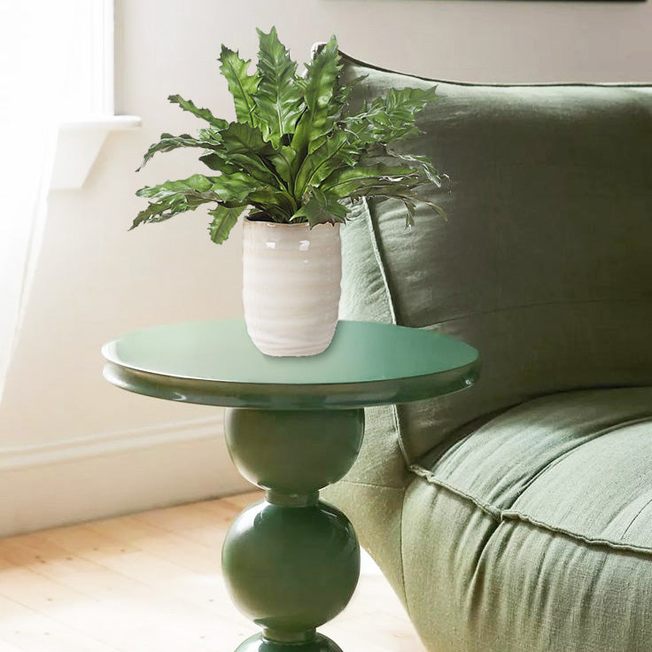 Faux fern on a green accent table with green sofa.