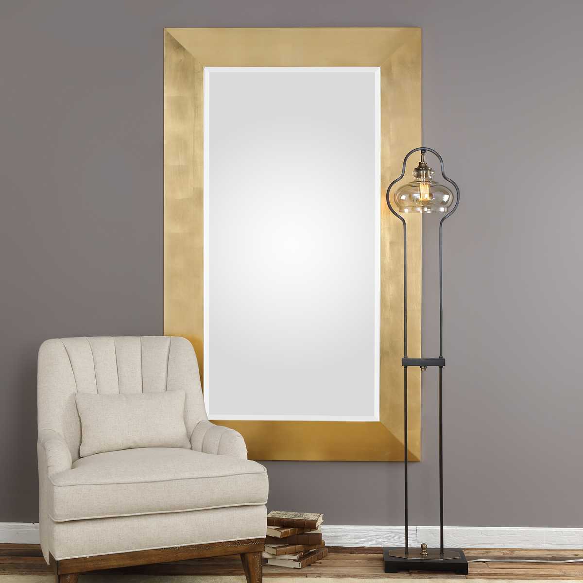 Gold-framed mirror above a beige armchair with a floor lamp in a room.