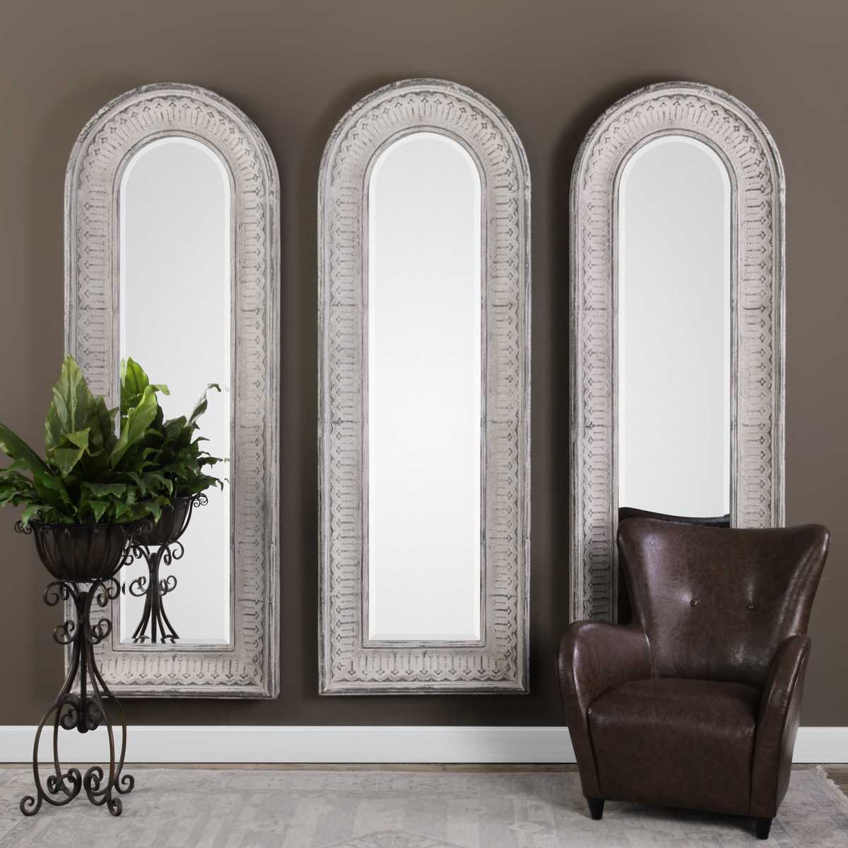 Three decorative mirrors with ornate frames on a wall, accompanied by a brown leather chair and a potted plant.
