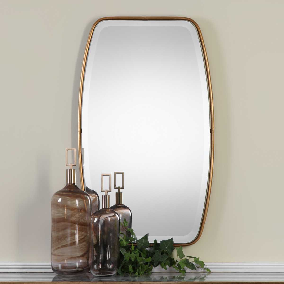 Rectangular mirror with gold frame on a wall above a shelf with decorative bottles and plants.
