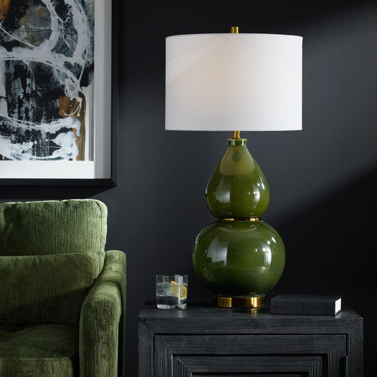 Green gourd lamp on books with a beige armchair in a dimly lit room