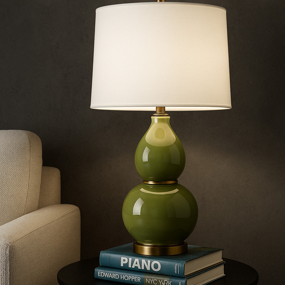 Green gourd lamp on books with a beige armchair in a dimly lit room