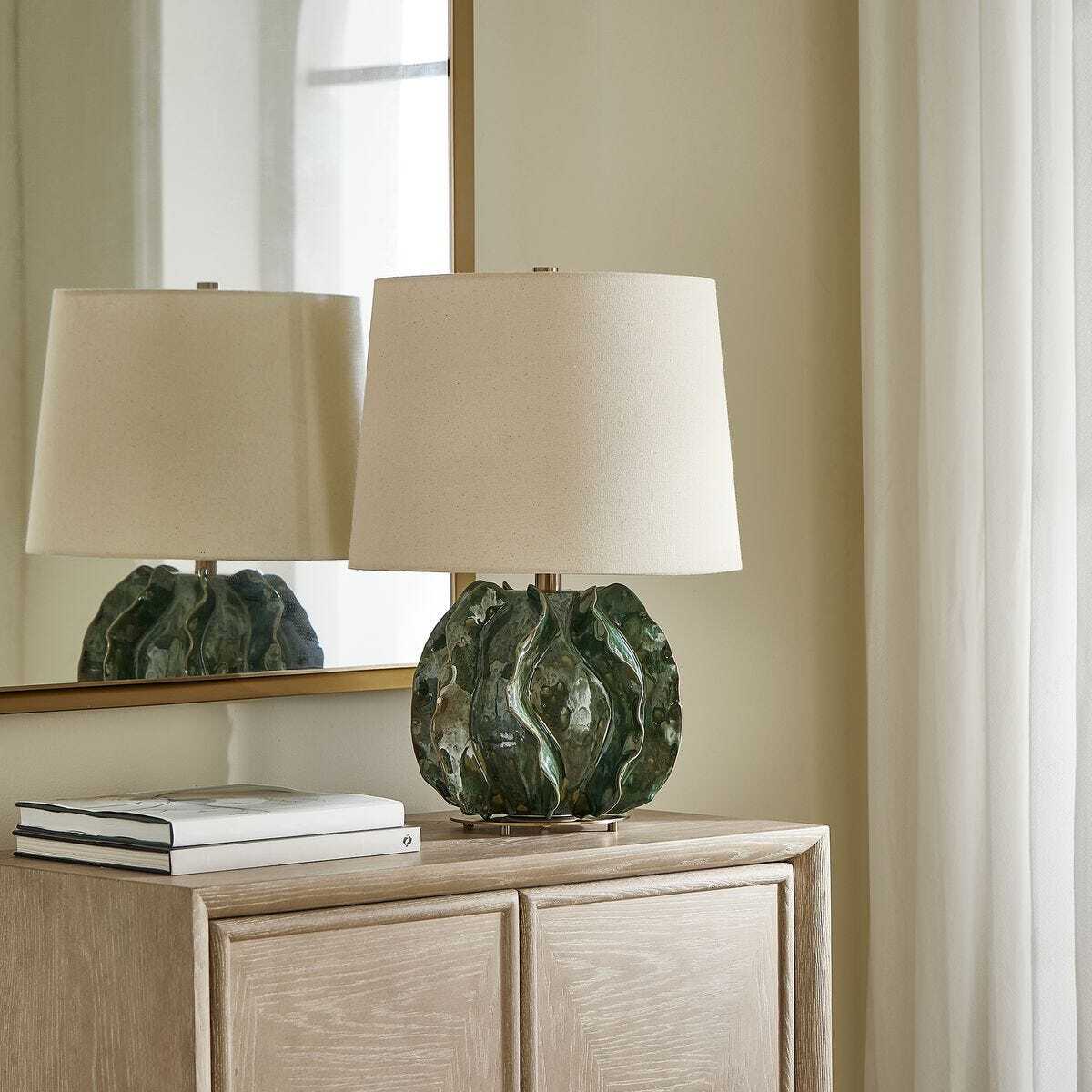 Decorative lamp with green base on a wooden cabinet next to a mirror.