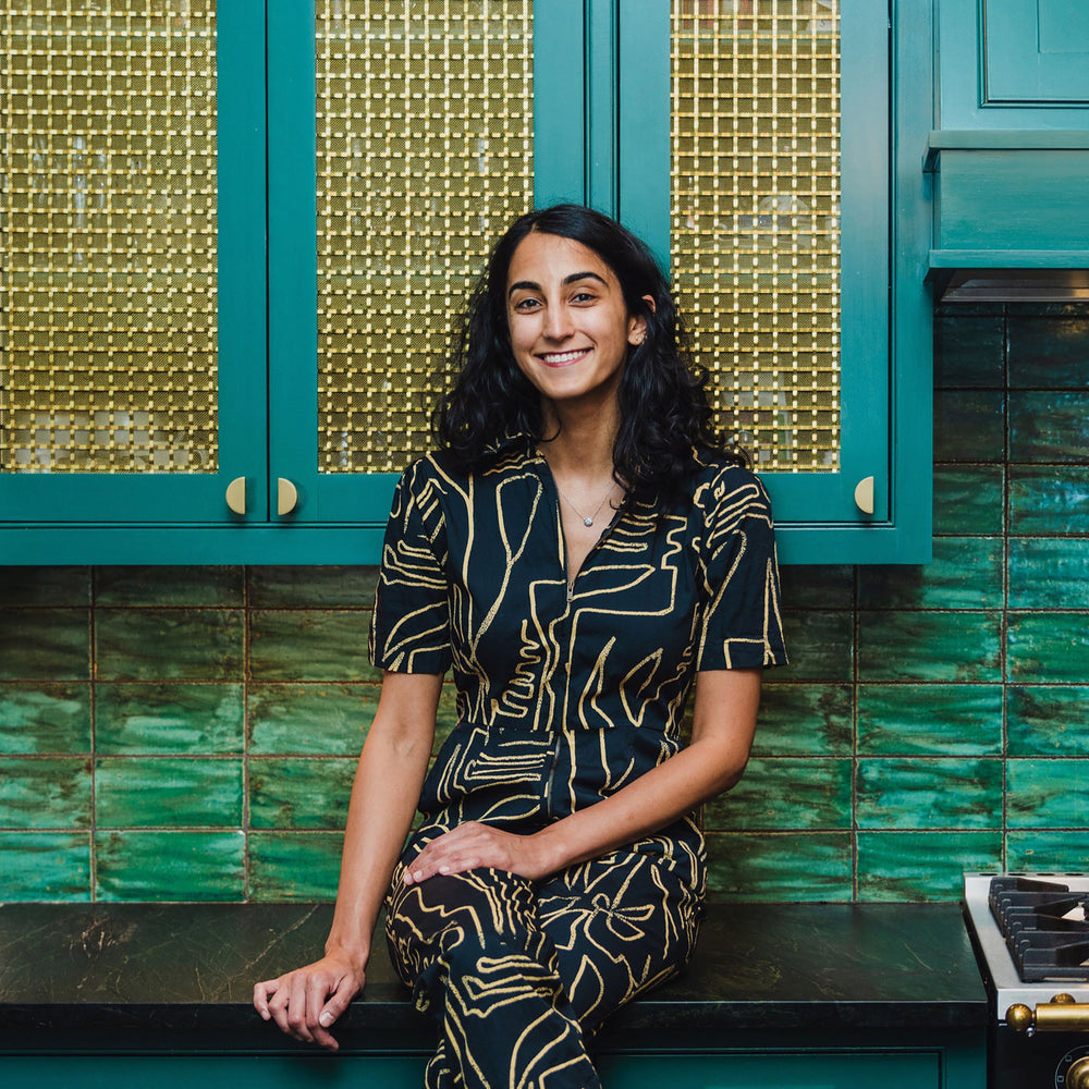 Woman sitting on a kitchen counter with teal cabinets and green tiles.
