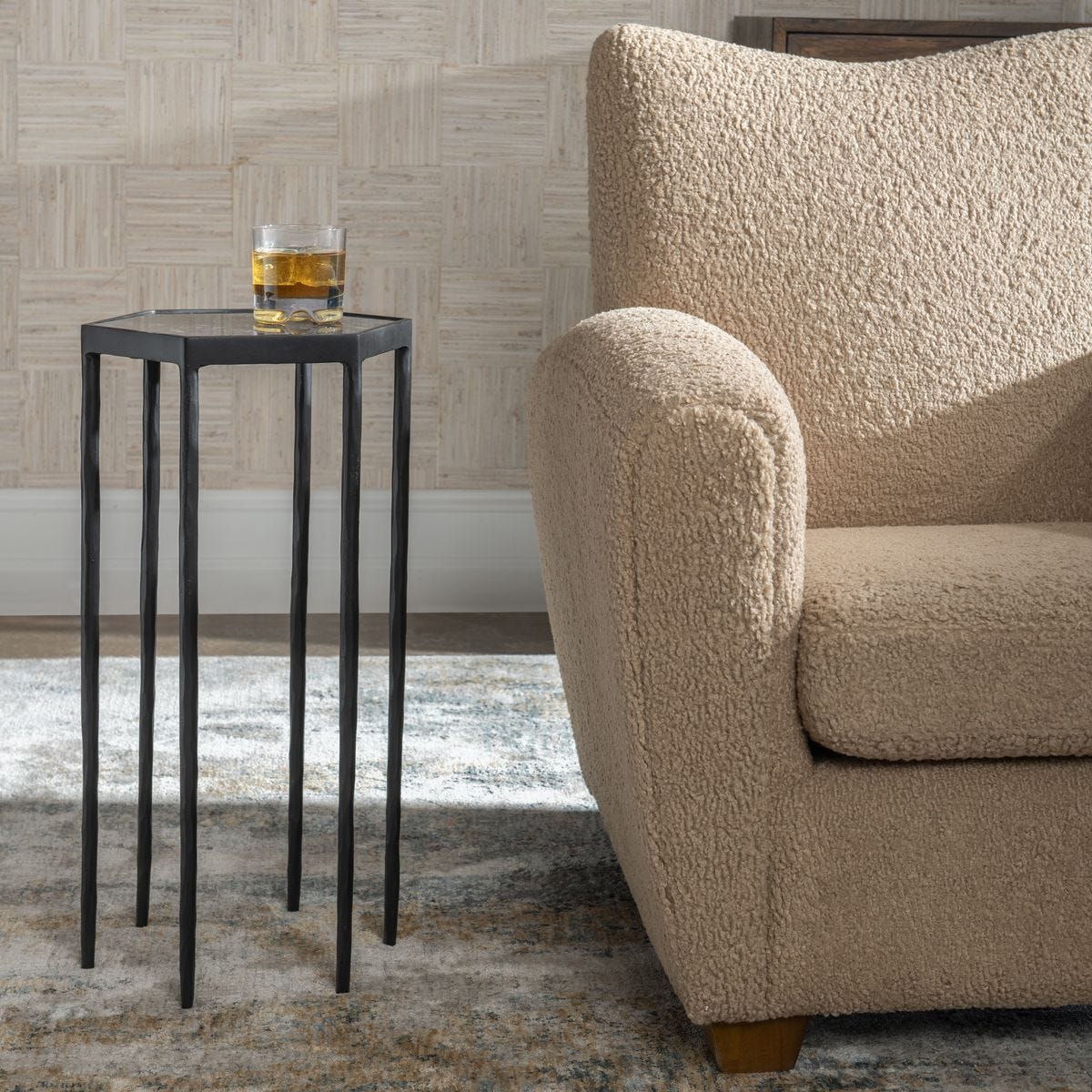 Beige textured sofa next to a black side table with a glass of whiskey on a patterned rug.