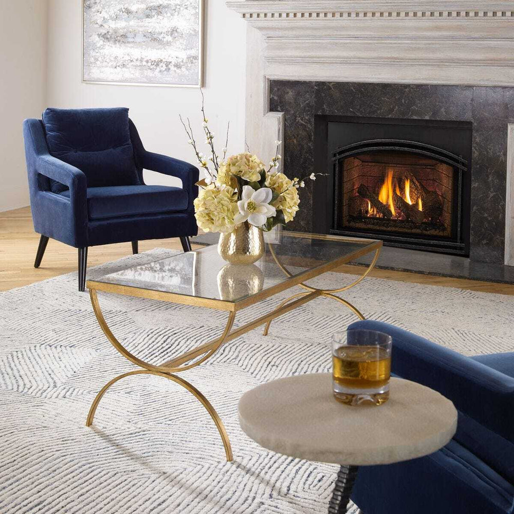 Living room with a fireplace, blue armchair, glass coffee table, and decorative items.