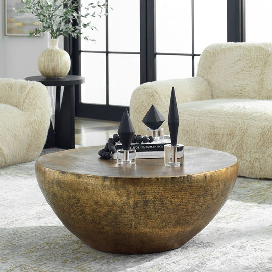 A beautifully hammered aluminum and an antique gold finish coffee table in front of an off-white sofa.