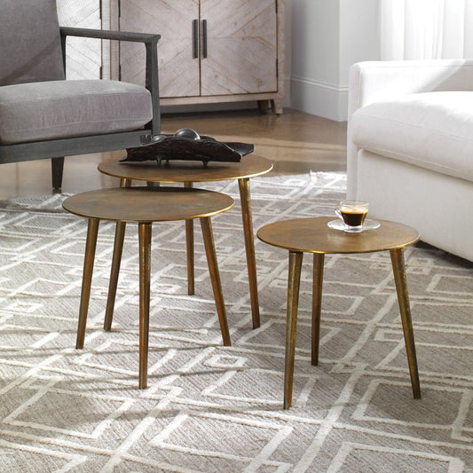 Set of three nesting coffee tables are made from cast aluminum with noticeable texture and are finished in oxidized antique gold next to white sofa.