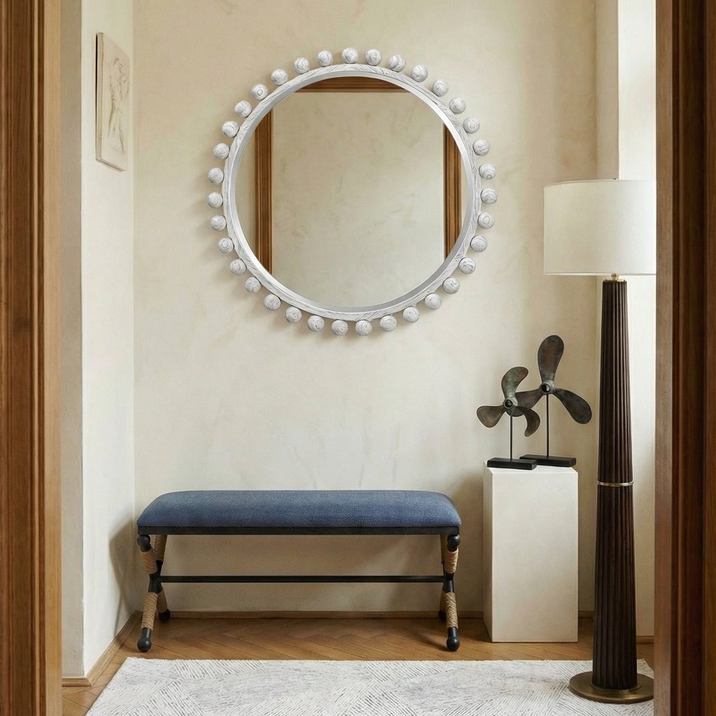 Entryway with round mirror, blue bench, and lamp on a beige wall.