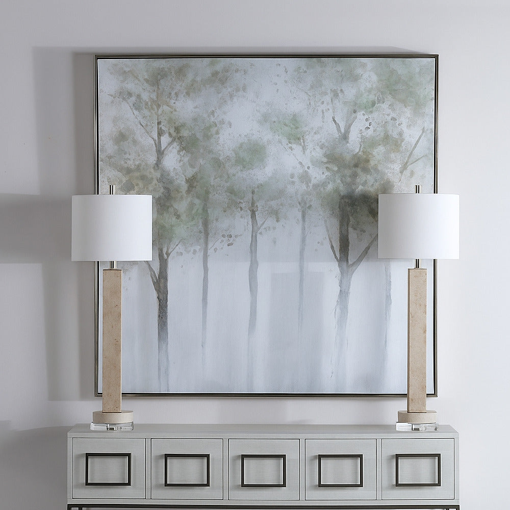 Framed abstract artwork above a console table with two lamps.