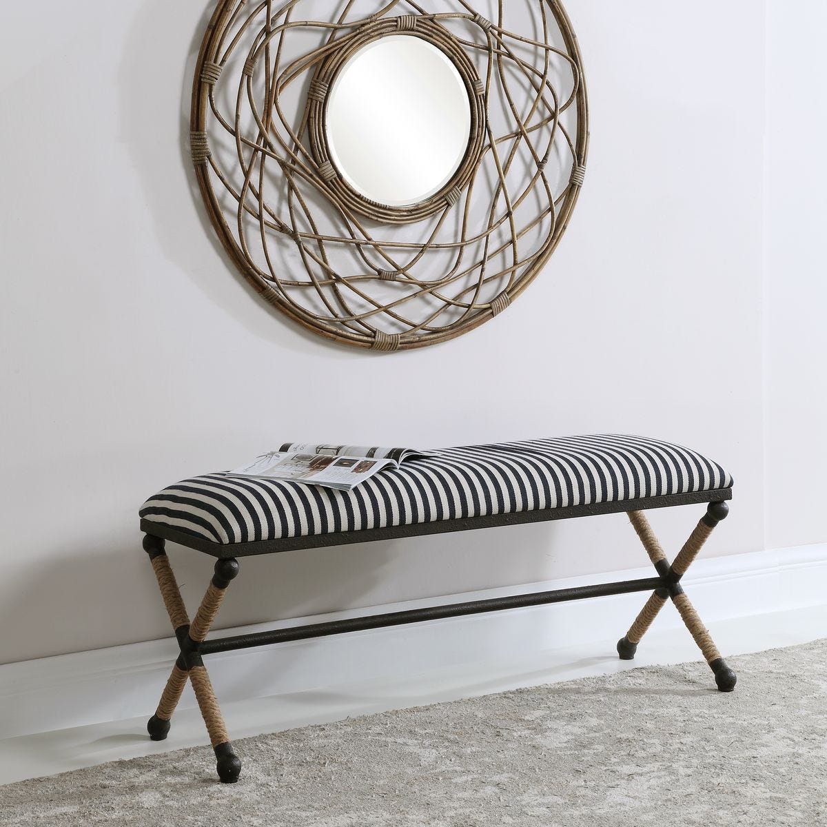 Striped bench with woven legs against a white wall with a decorative mirror.